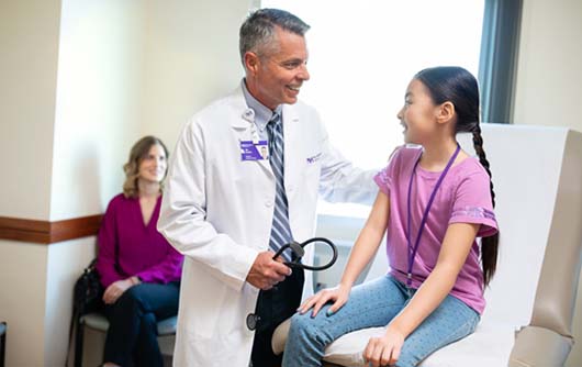 A male physician discussing proton therapy with a young female patient and her mom.