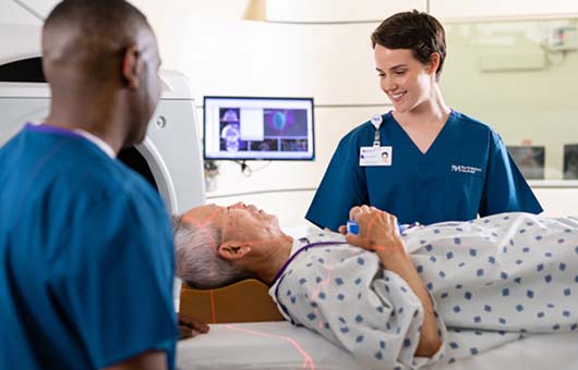 Two proton therapy technicians preparing a male patient for treatment.