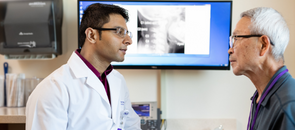 A male doctor talking with an elderly male patient with an X-ray image of a neck in the background.