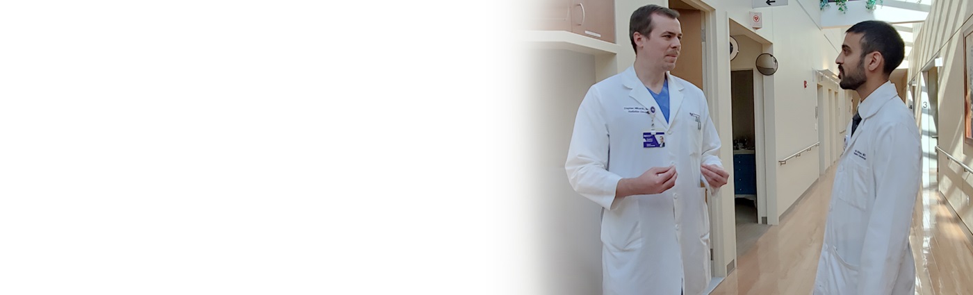 Two male Proton physicians standing in a hallway while talking to each other.