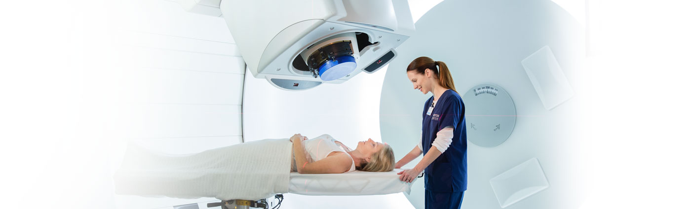 A female employee gets a female patient setup on a table for proton therapy.