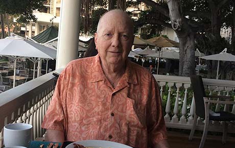 An elderly man eating breakfast and smiling.